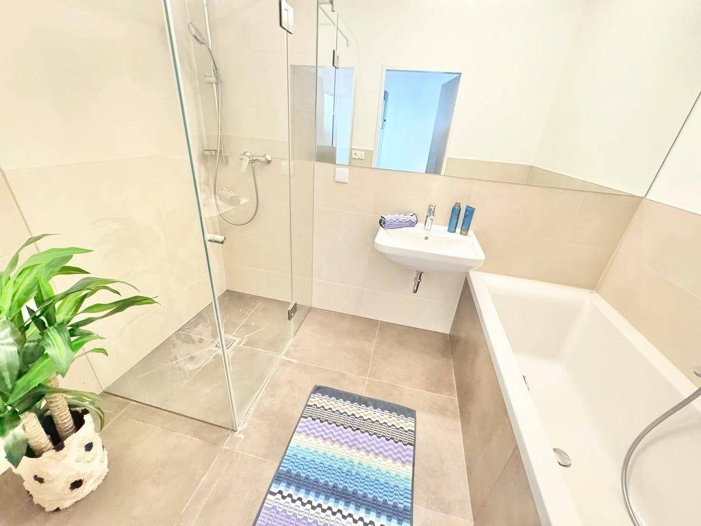 Modernes Badezimmer mit Badewanne, ebenerdiger Dusche und großem Spiegel, in hellen Fliesen gehalten.