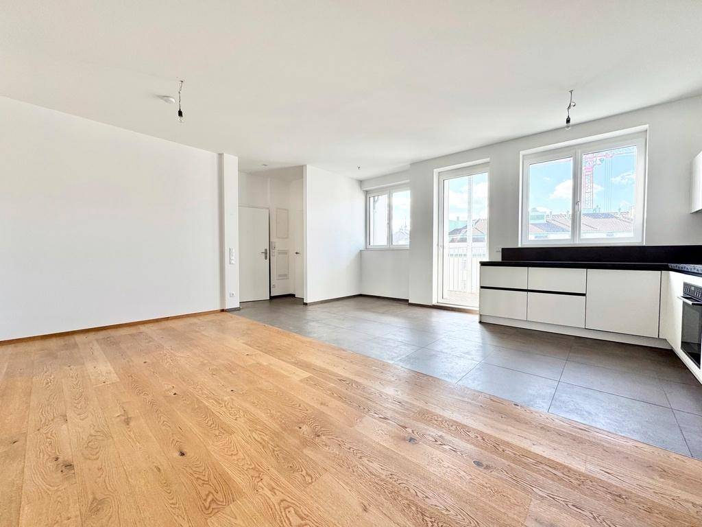 Geräumiger Wohnbereich mit integrierter Küche, hellen Wänden und Zugang zum Balkon durch eine Fenstertür.