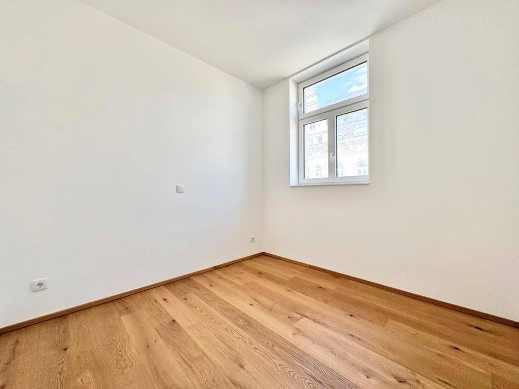 Geräumiges Zimmer mit hellem Parkettboden und einem großen Fenster, das viel Tageslicht hereinlässt.
