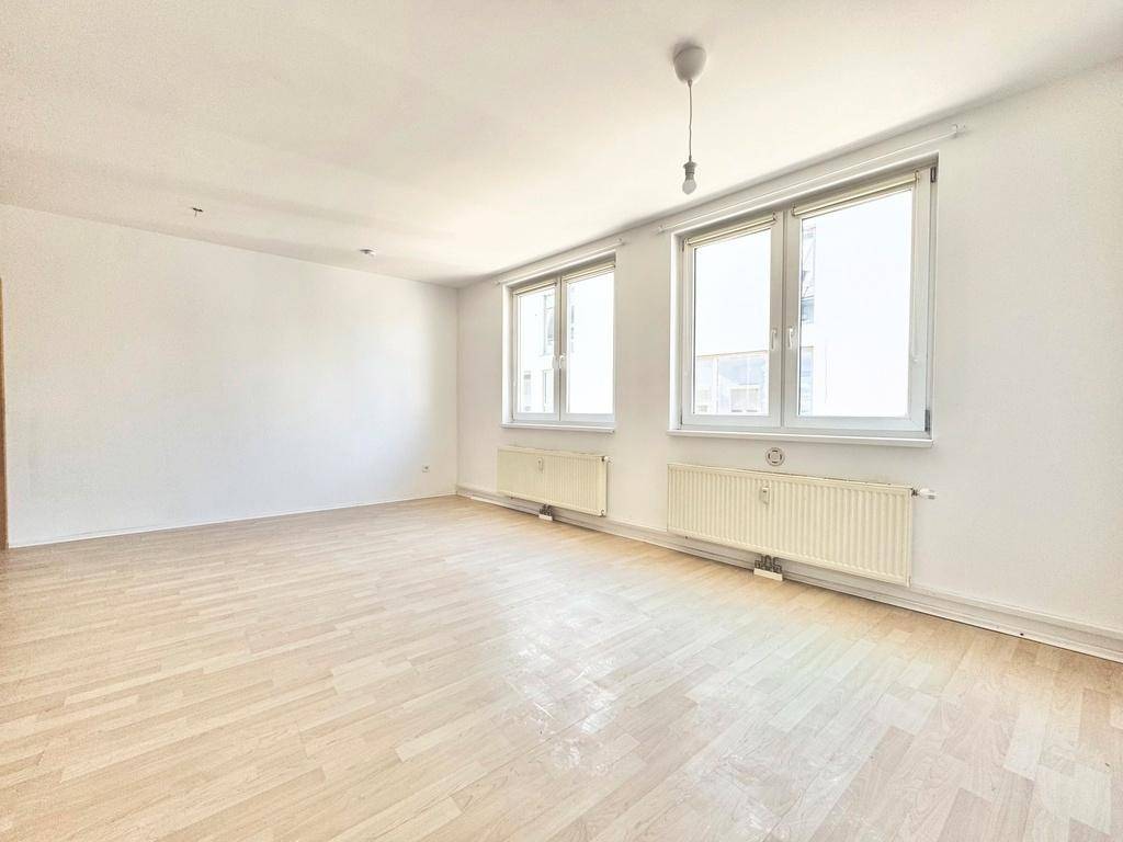 Geräumiges, helles Zimmer mit Holzboden und zwei Fenstern, bereit zur individuellen Gestaltung.