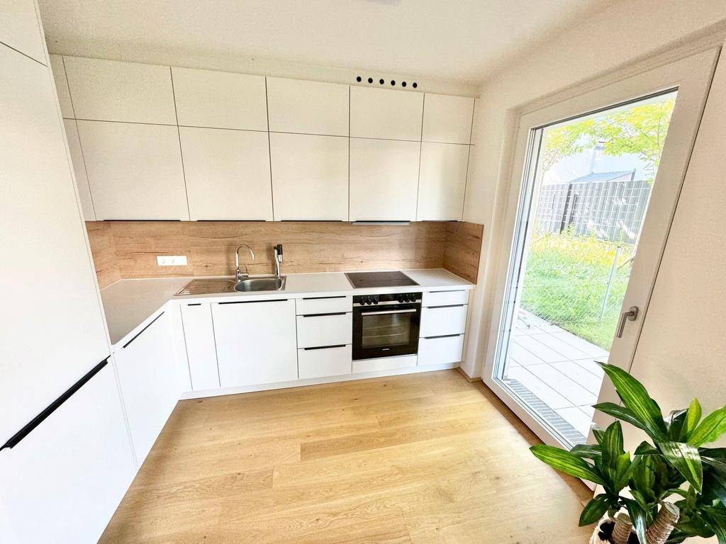 Moderne Einbauküche mit weißen Fronten, Holzakzenten und direktem Zugang zur Terrasse.