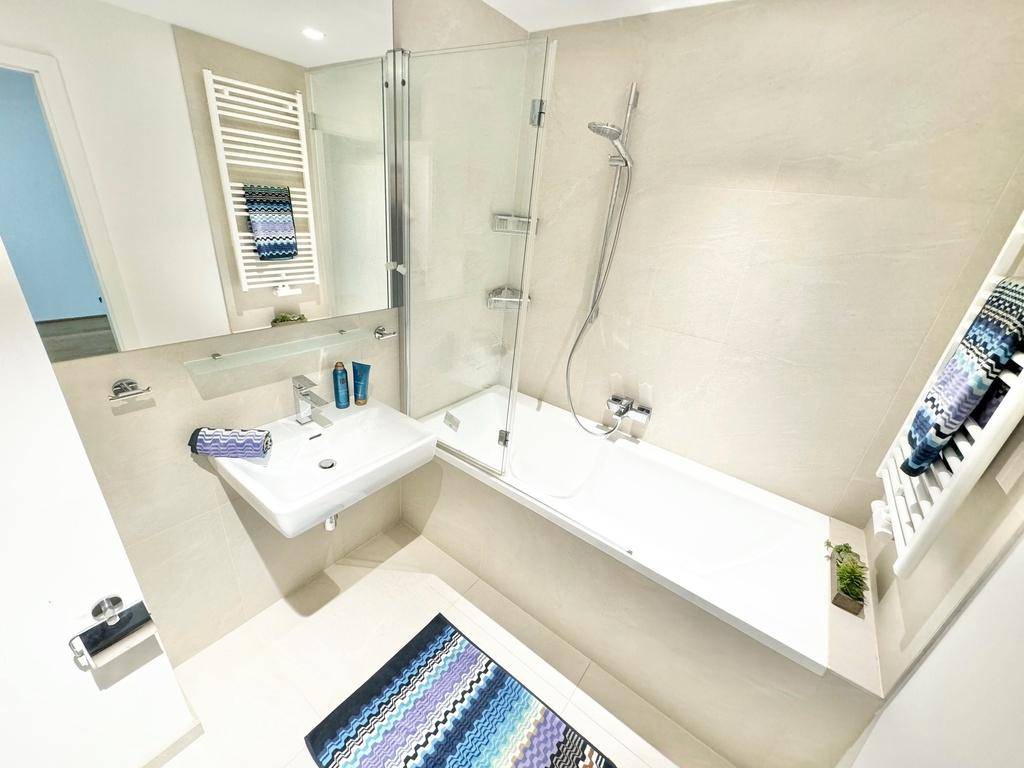 Modernes Badezimmer mit Badewanne, Duschbereich, Einzelwaschbecken und Handtuchheizkörper.