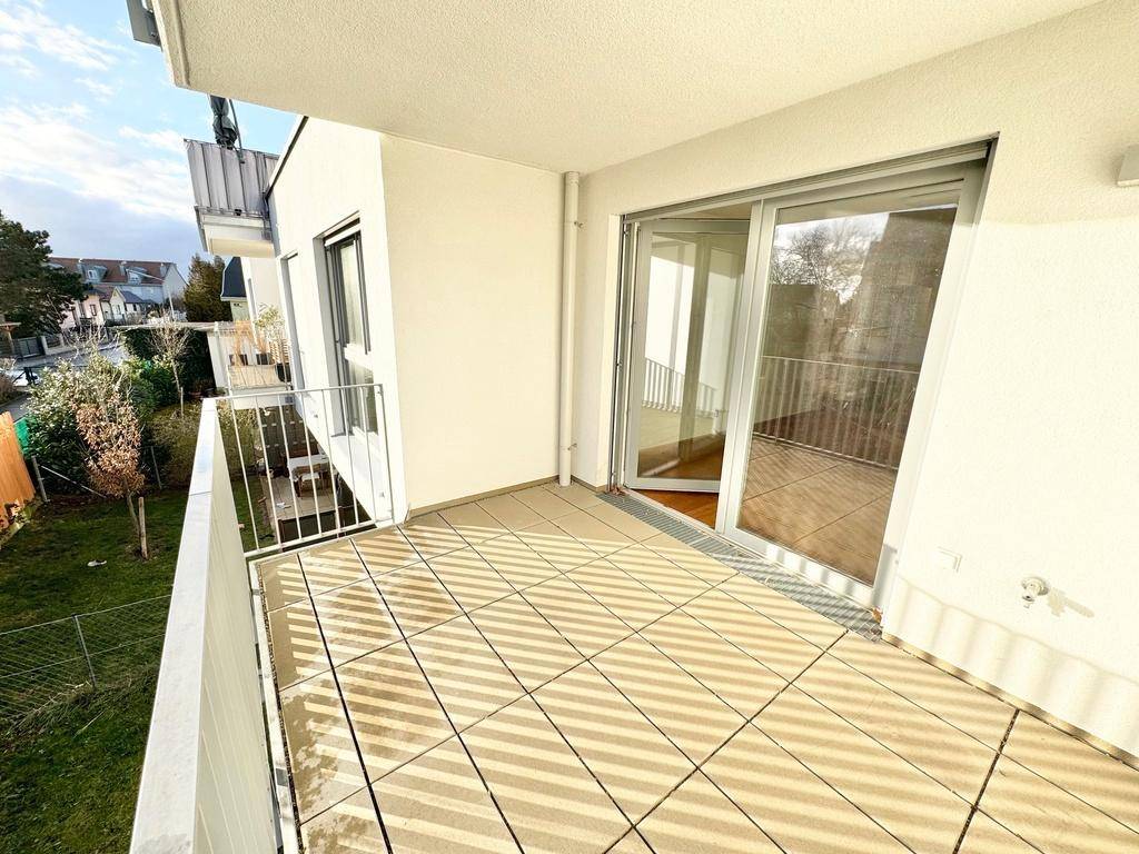 Heller Balkon mit Zugang zum Innenbereich durch eine große Glasschiebetür und Blick auf die Umgebung.
