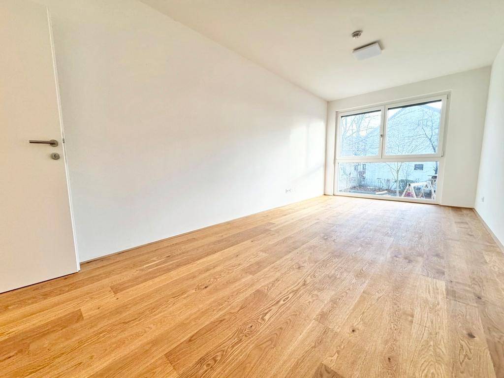 Helles Schlafzimmer mit neuem Holzparkettboden und großem Fenster mit Blick ins Grüne.
