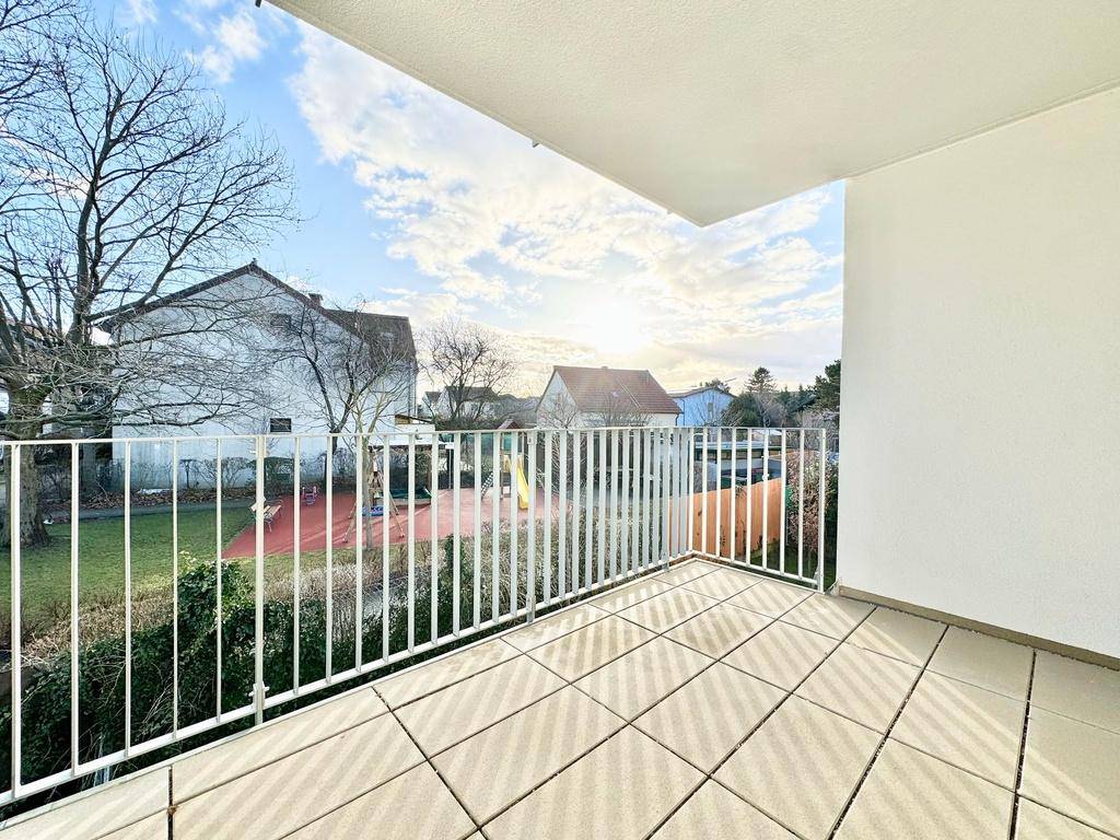 Heller Balkon mit Fliesenboden und weitem Blick über den grünen Innenhof und die Nachbarschaft.
