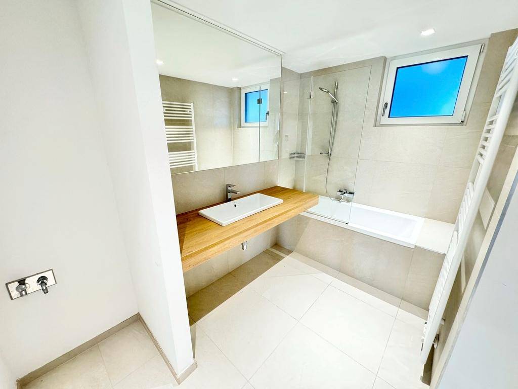Helles Badezimmer mit modernen Armaturen, Badewanne, Holzwaschtisch und einem Fenster für Tageslicht.