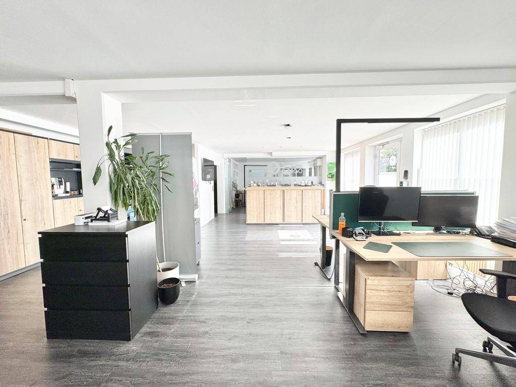 Großes, offenes Büro mit dunklem Boden, weißen Wänden und modernen Holzmöbeln, gut beleuchtet.