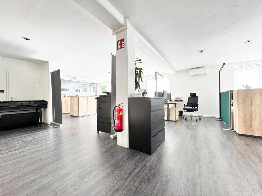 Offenes Büro mit einer tragenden Säule, einem Feuerlöscher und verschiedenen Bürogeräten, gut beleuchtet.