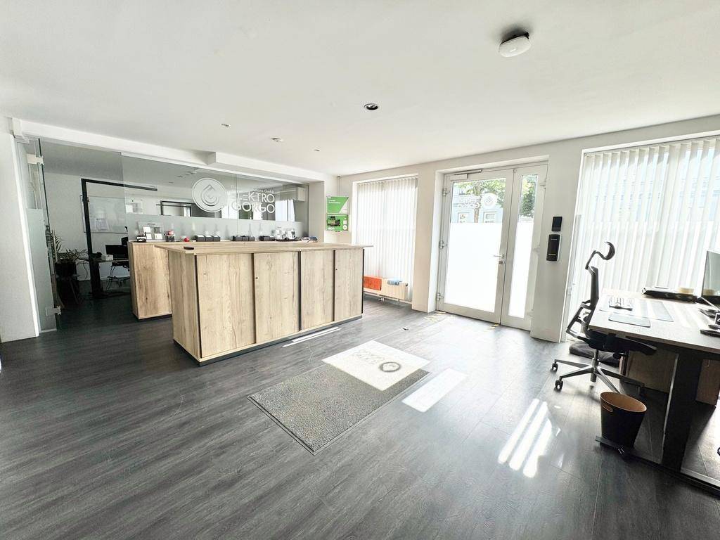 Empfangsbereich eines Büros mit einem Holzschalter, dunklem Boden und großen Fenstern mit vertikalen Jalousien.