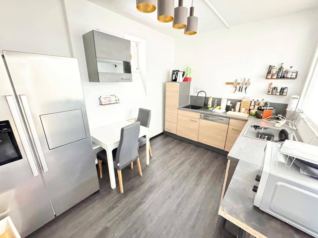 Moderne Küche mit hellen Holzschränken, einem großen Kühlschrank und einem kleinen Esstisch, gut ausgestattet.
