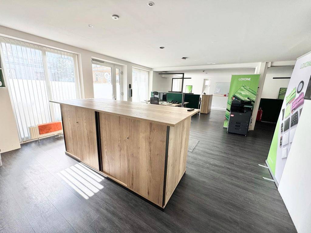 Büroraum mit einer Holztheke, großen Fenstern und Werbebannern im Hintergrund, hell und modern.