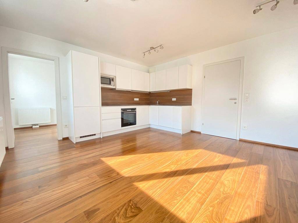 Moderner Wohnbereich mit integrierter Küche, Holzboden und viel natürlichem Lichteinfall.