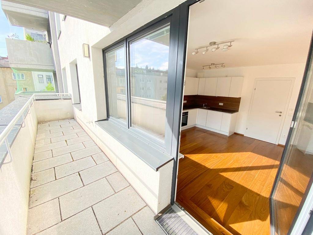 Balkon mit Fliesenboden und direktem Zugang zu einem hellen Wohnbereich mit Holzboden.