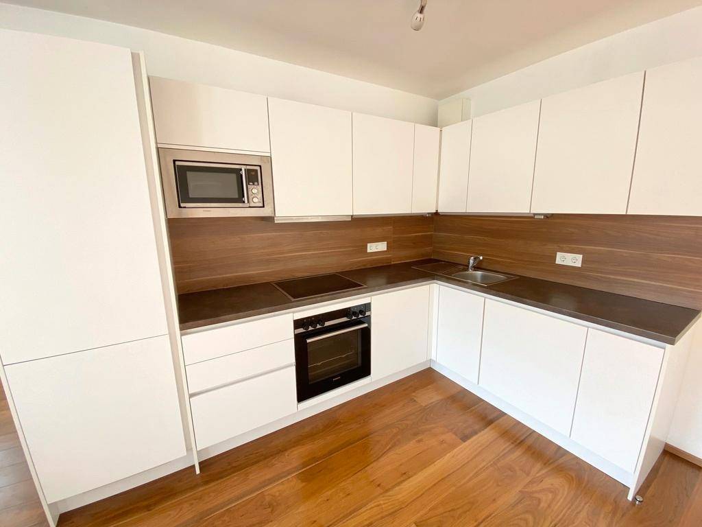 Moderne Einbauküche mit weißen Schränken, dunkler Arbeitsplatte und integrierten Geräten.