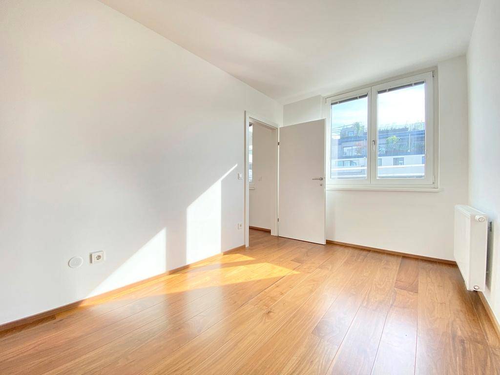 Helles Schlafzimmer mit Holzboden, weißen Wänden und Fenster für Tageslicht.