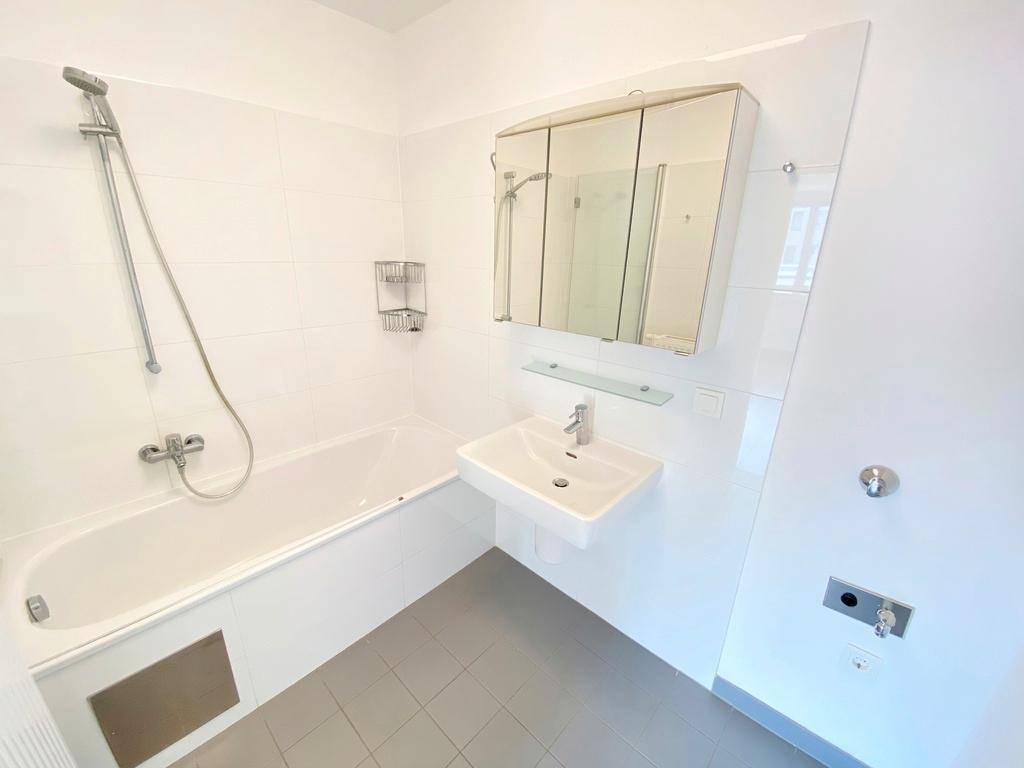 Modernes Badezimmer mit Badewanne, Waschbecken, Spiegelschrank und weißen Fliesen.