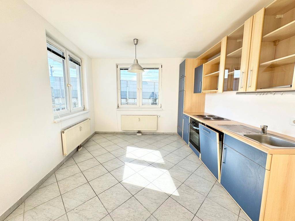 Funktionale Küche mit blauen und holzfarbenen Schränken, Fliesenboden und Fenster.