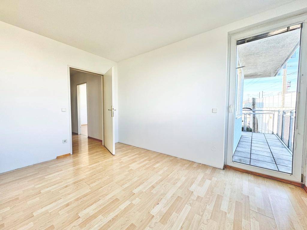 Helles Zimmer mit Parkettboden und direktem Zugang zu einem Balkon.