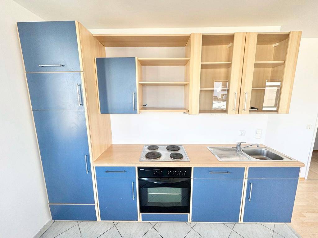 Detailansicht der Einbauküche mit blauen Fronten, Holzdetails und grundlegenden Geräten.