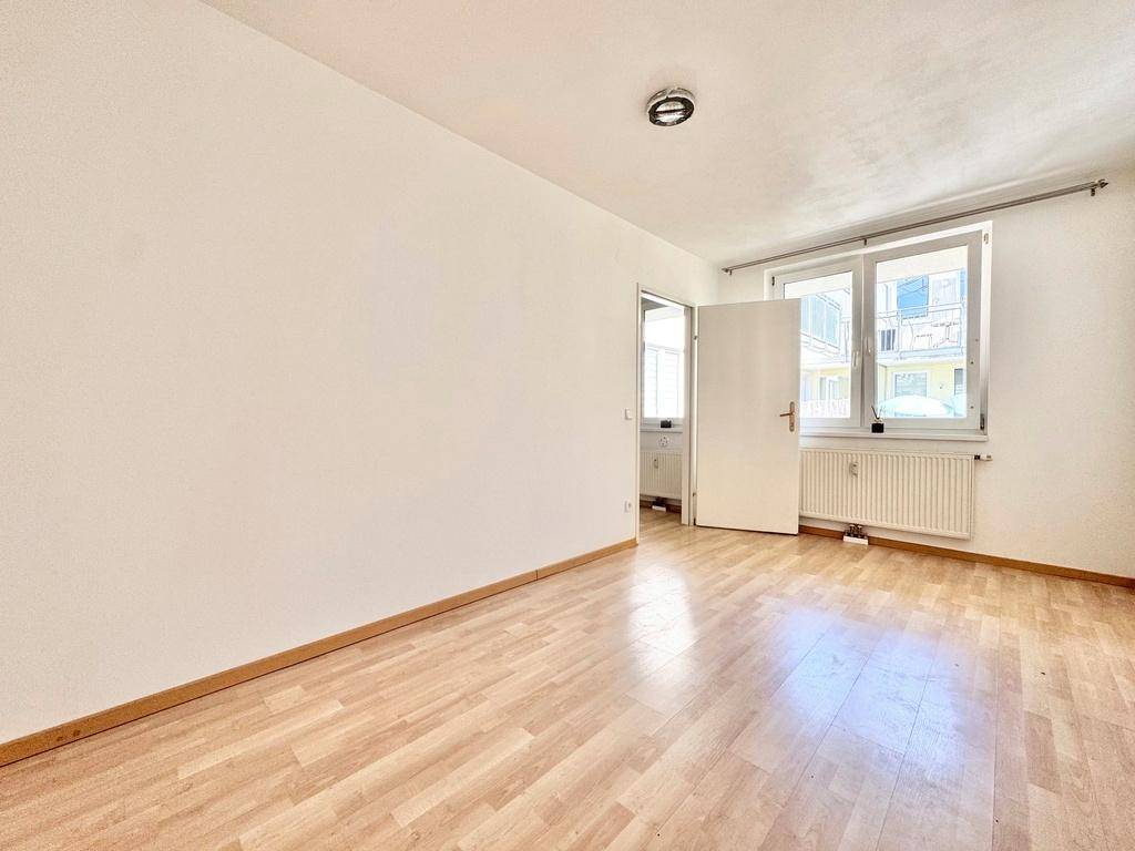 Freundliches Zimmer mit Laminatboden, großen Fenstern und viel Tageslicht.
