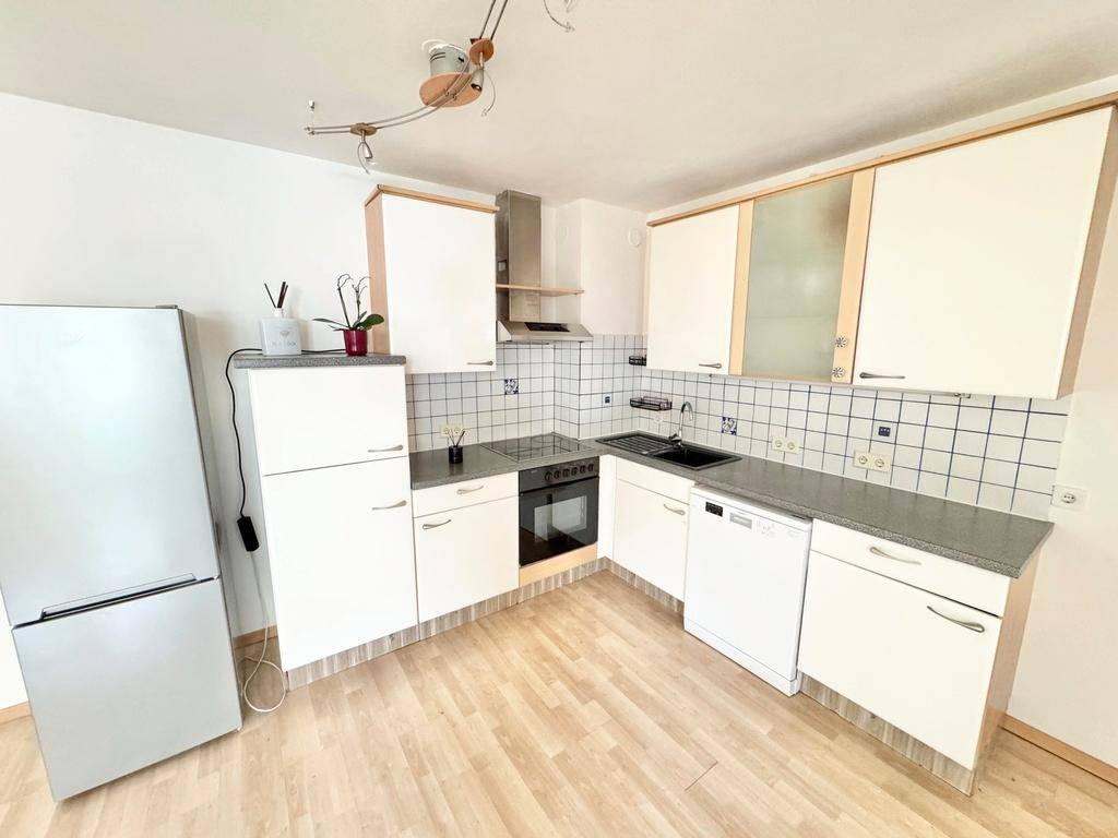 Funktionale Einbauküche mit weißen Schränken, Fliesenrückwand und modernen Geräten.