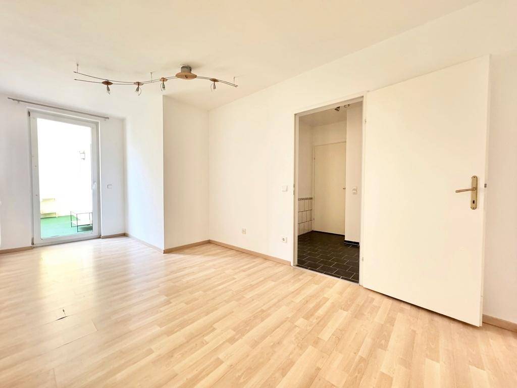 Helles Zimmer mit Laminatboden, weiß gestrichenen Wänden und Zugang zu einem gefliesten Flur.