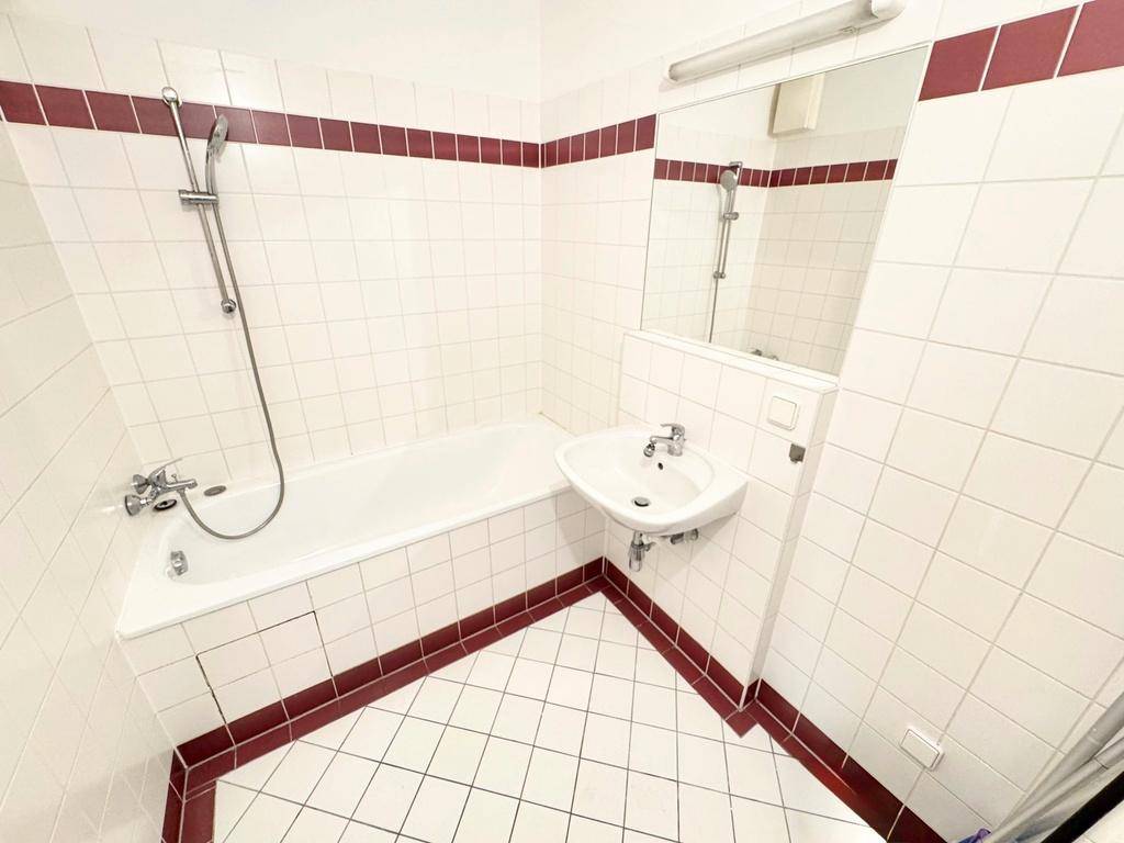 Badezimmer mit Badewanne, Duschfunktion, Waschbecken und weiß-roten Fliesen.