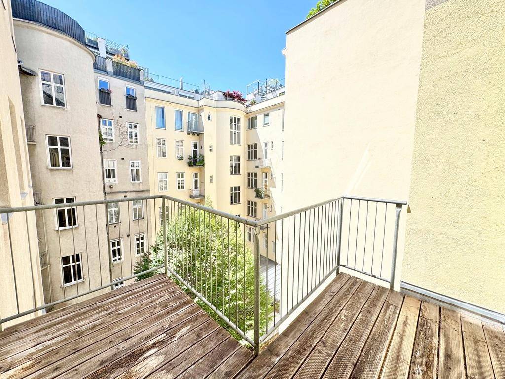 Balkon mit Holzfußboden und Metallgeländer, der einen Blick auf den begrünten Innenhof bietet.