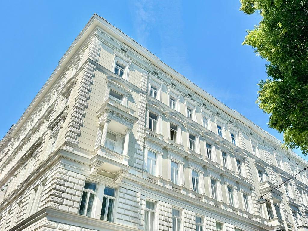 Prächtige Fassade eines Altbaus mit reich verzierten Details und vielen Fenstern unter blauem Himmel.