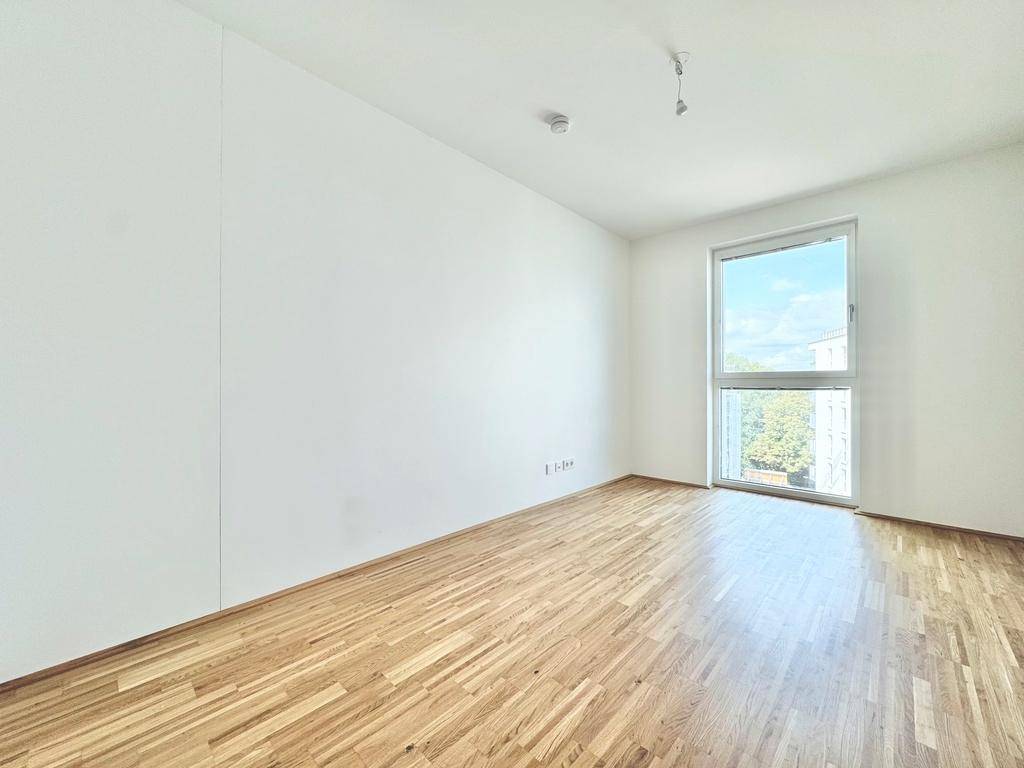 Helles Zimmer mit Parkettboden und großem Fenster, ideal als Schlaf- oder Arbeitszimmer.