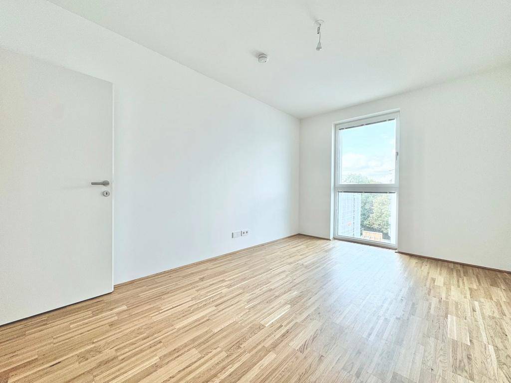 Helles Schlafzimmer mit Parkettboden und großem Fenster, bereit zur individuellen Gestaltung.