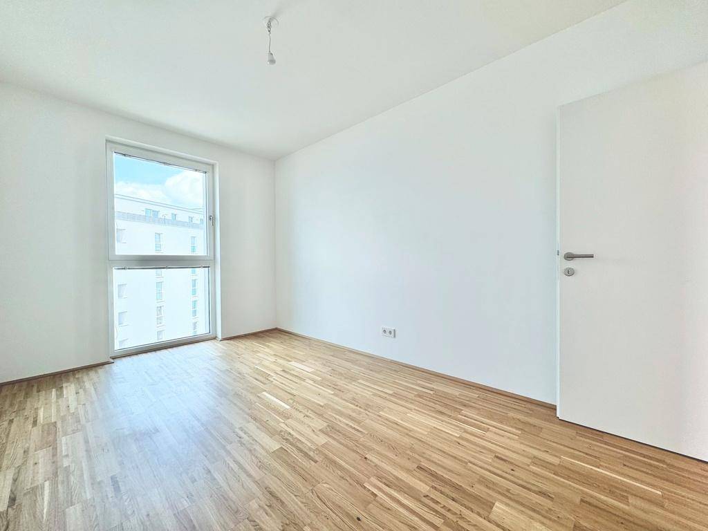 Geräumiges Schlafzimmer mit hellem Parkettboden und viel Tageslicht durch das Fenster.
