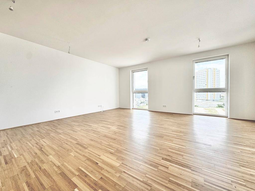 Geräumiger Wohnraum mit Eichenparkett und großen Fenstern, die viel Licht hereinlassen.