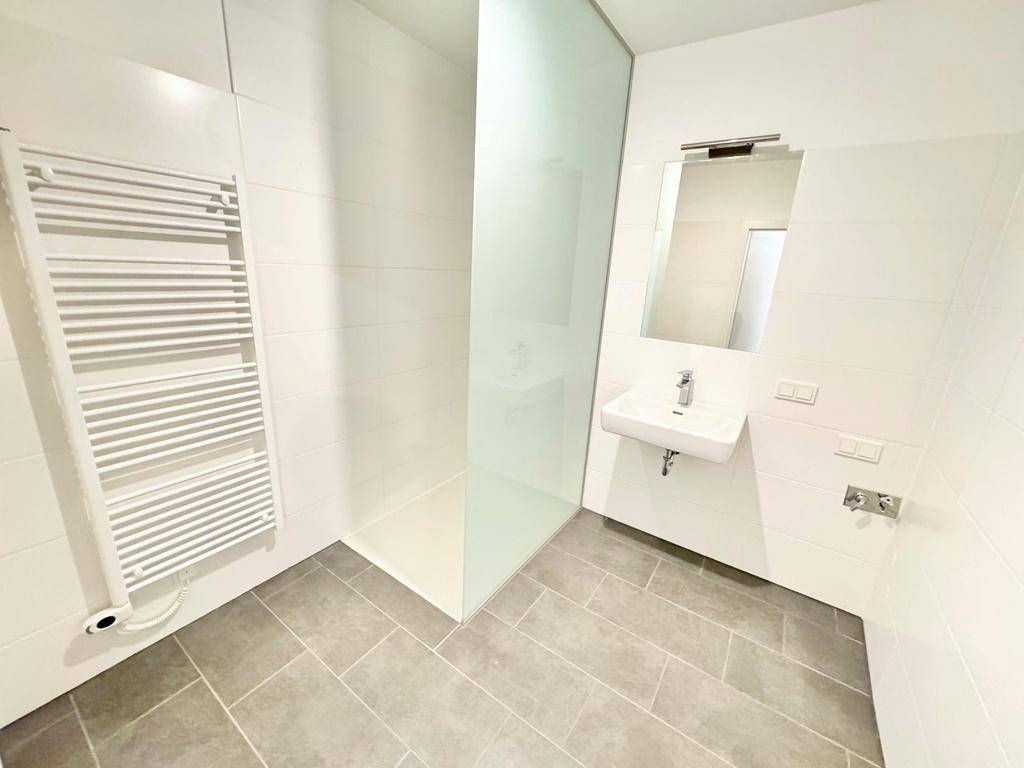 Modernes Badezimmer mit ebenerdiger Dusche, Handtuchheizkörper und hellen Fliesen.