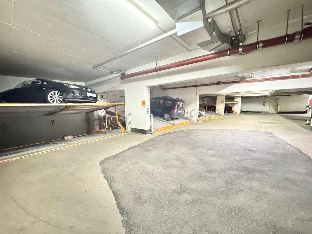 Weitläufige Tiefgarage mit mehreren automatischen Parkliftsystemen und geparkten Fahrzeugen.