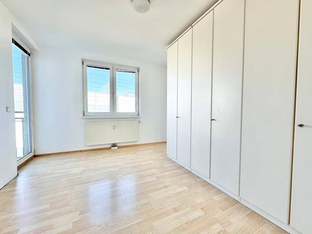 Geräumiges Schlafzimmer mit Einbauschränken, Parkettboden und großem Fenster.