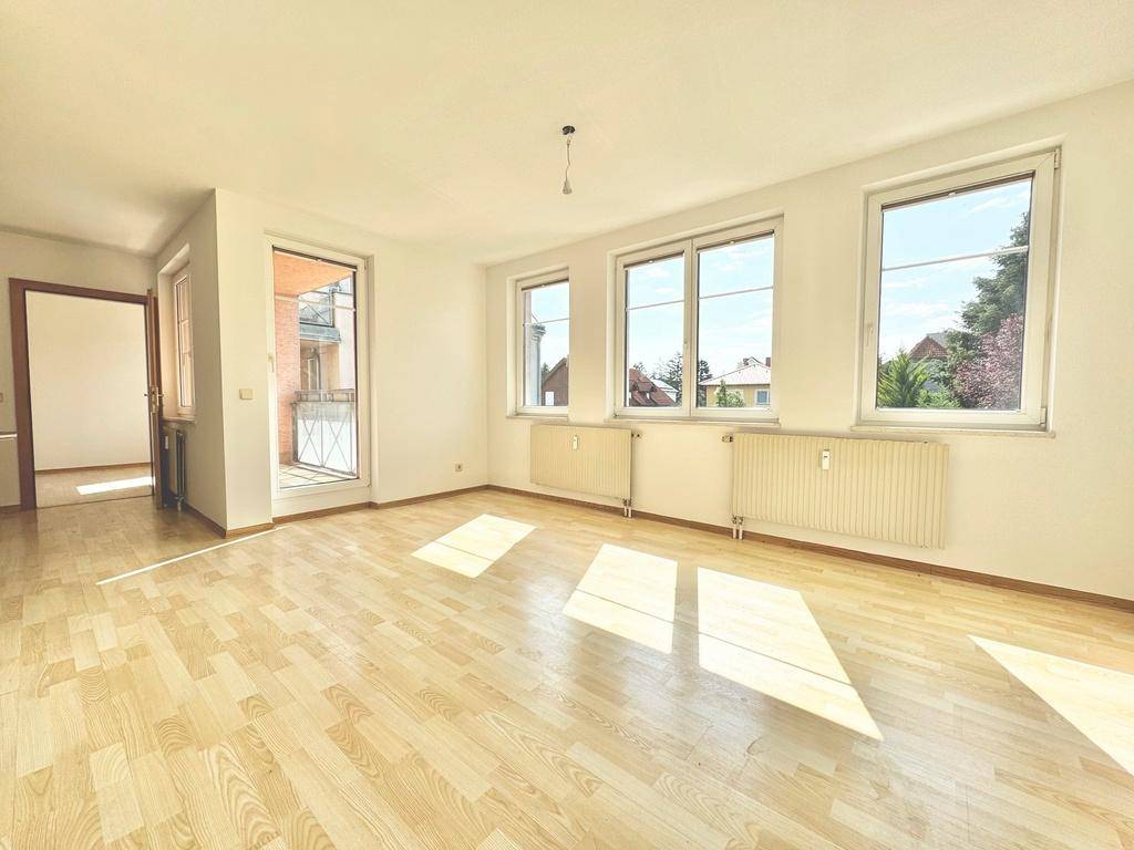 Helles und geräumiges Wohnzimmer mit Parkettboden, großen Fenstern und Zugang zum Balkon.