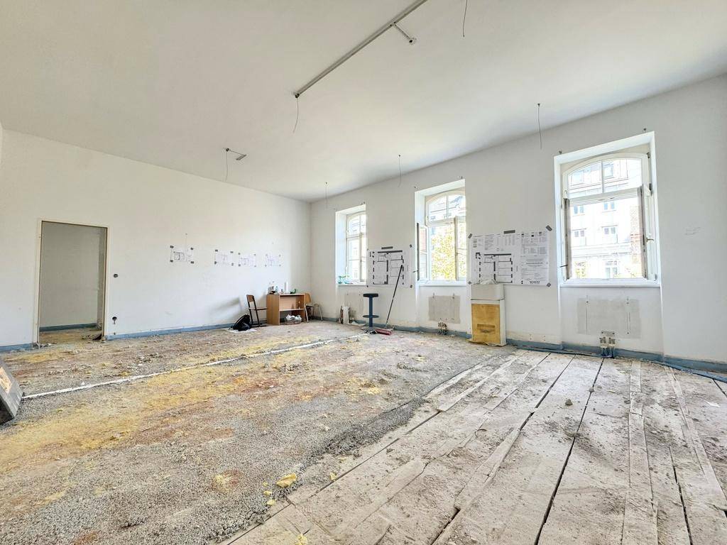 Geräumiger Innenraum in Renovierungsphase mit sichtbaren Holzdielen und Tageslicht von außen.