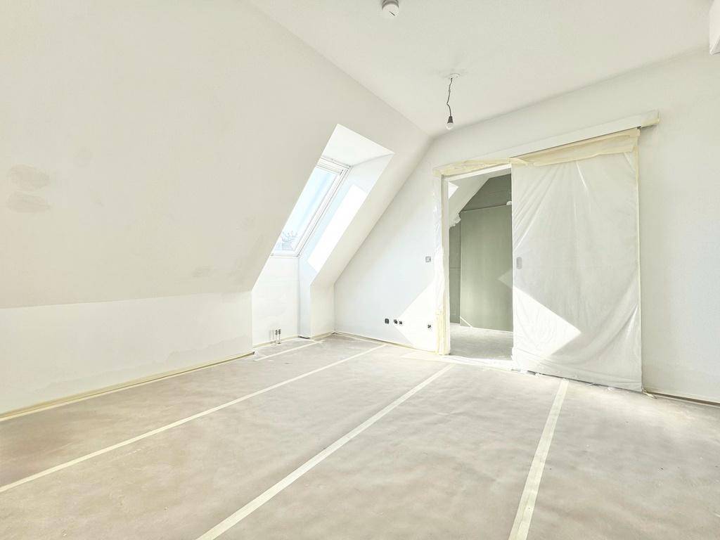 Heller Dachgeschossraum mit Schrägen, einem Dachfenster und einer breiten Schiebetür zu einem Nebenraum.