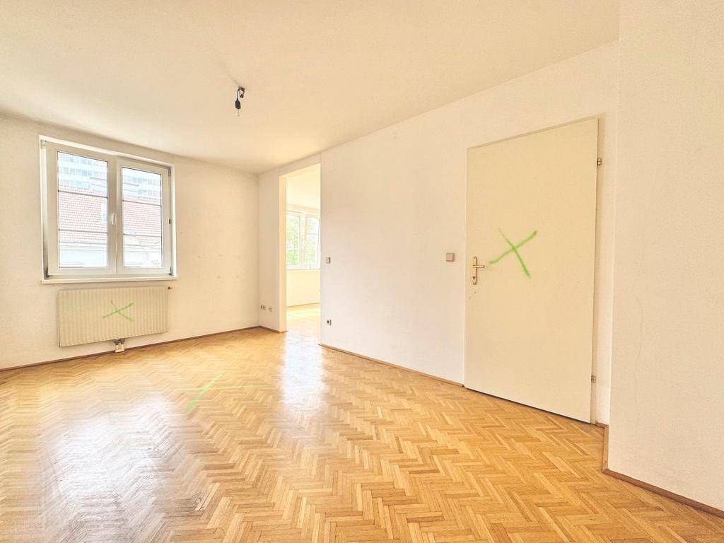 Heller Raum mit Fischgrätparkett, weißen Wänden und einem Fenster, das für natürliche Belichtung sorgt.