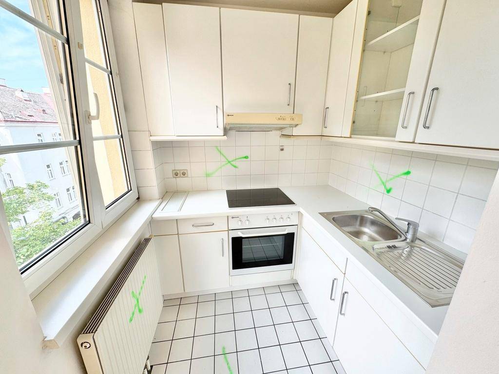 Funktionale Küche mit weißen Schränken, Fliesenboden und einem Fenster, das Tageslicht spendet.