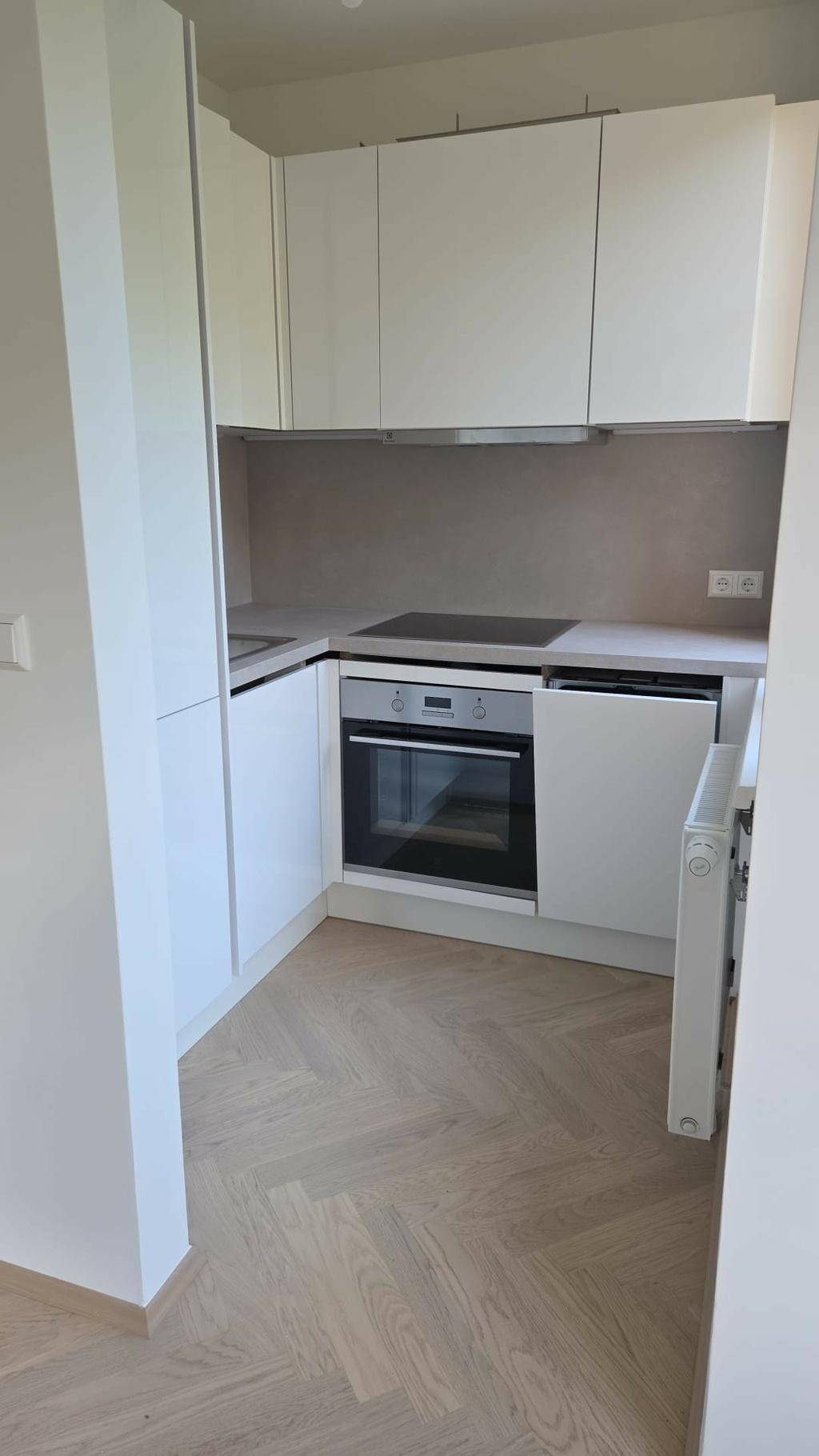 Moderne, kompakte Küche mit weißen, grifflosen Schränken, integriertem Backofen und hellem Parkettboden.
