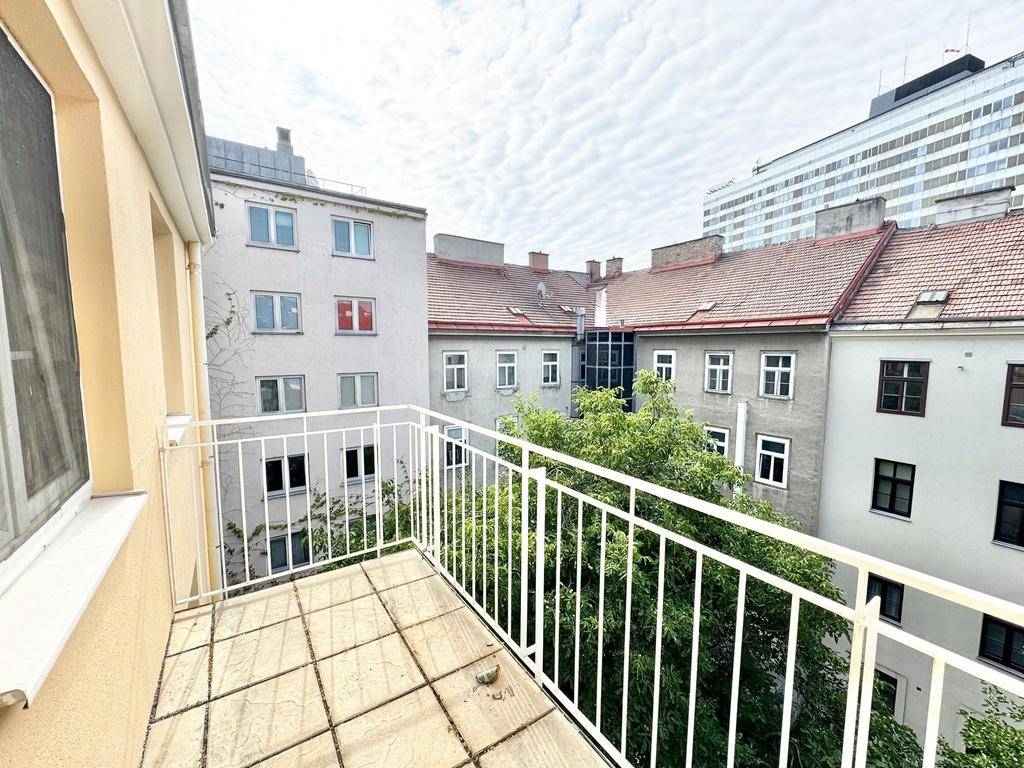 Heller Balkon mit Fliesenboden und weitem Blick über die umliegenden Gebäude und einen Baum.