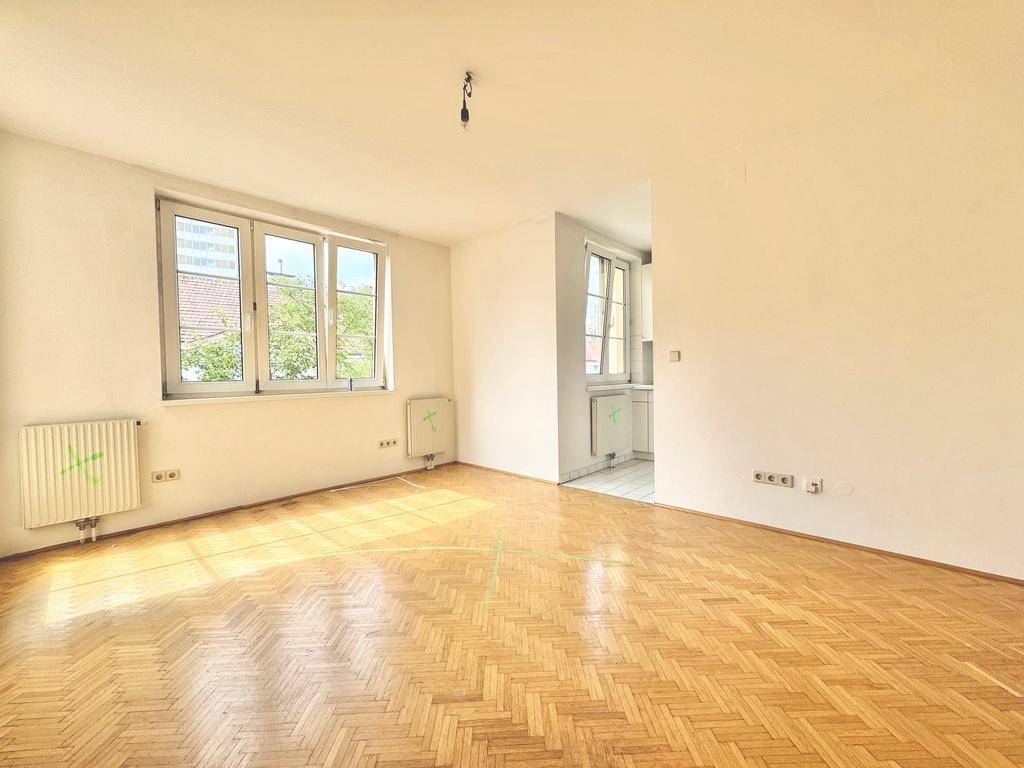 Helles Wohnzimmer mit Fischgrätparkett, weißen Wänden und großen Fenstern, die viel Tageslicht hereinlassen.