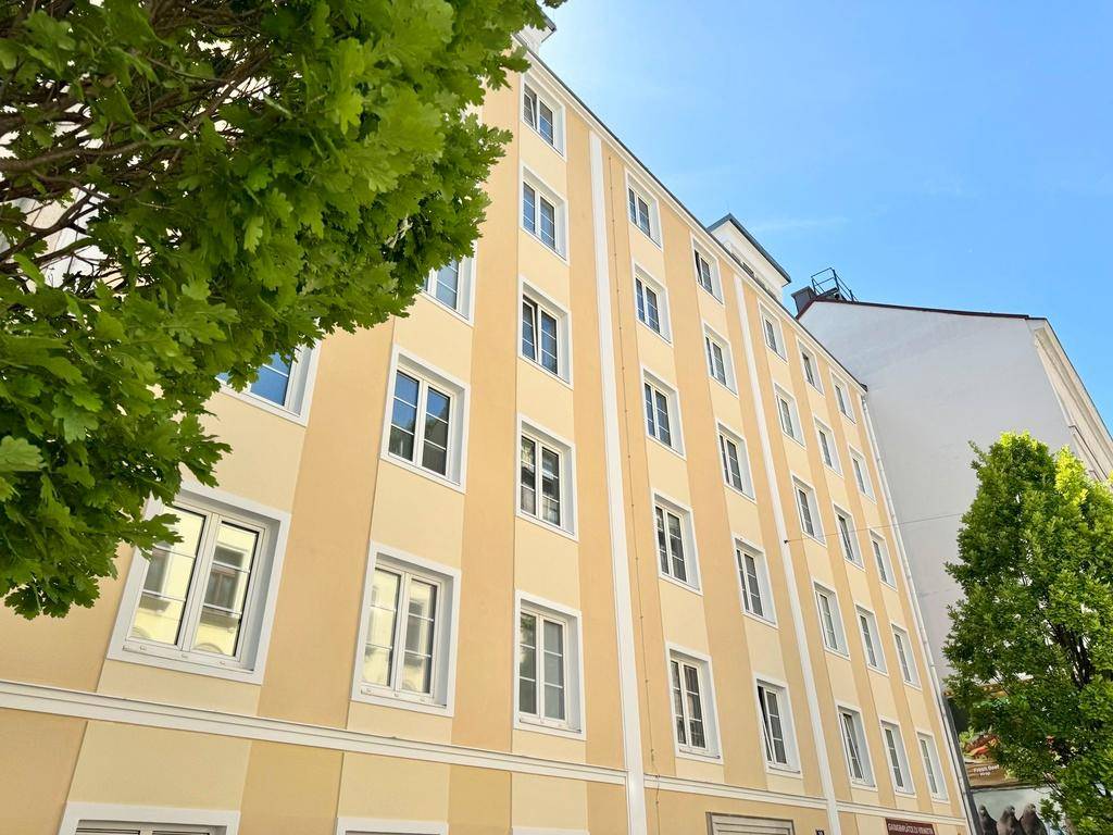 Mehrstöckiges Gebäude mit gelb-beiger Fassade und zahlreichen Fenstern unter blauem Himmel.