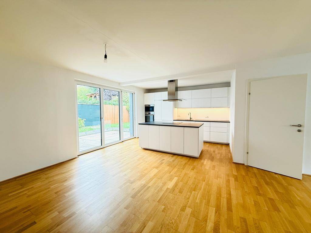 Heller offener Wohnbereich mit moderner Einbauküche, Kücheninsel und Zugang zur Terrasse.