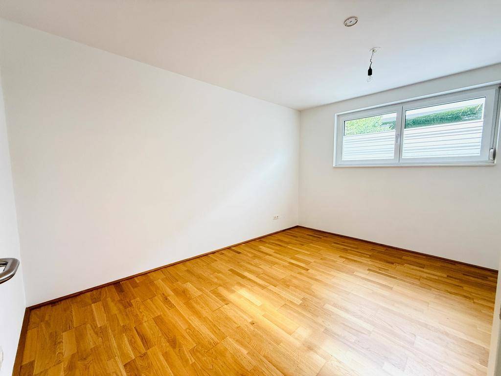 Helles Schlafzimmer mit Parkettboden und einem Fenster, das viel Tageslicht hereinlässt.