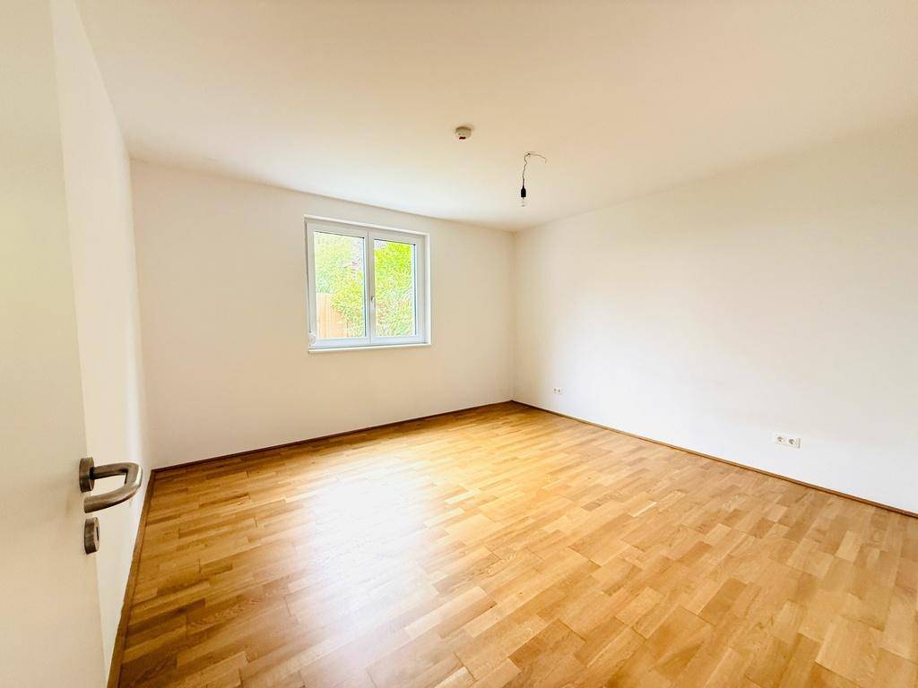 Leeres Zimmer mit Holzparkett und einem großen Fenster für natürliche Belichtung.