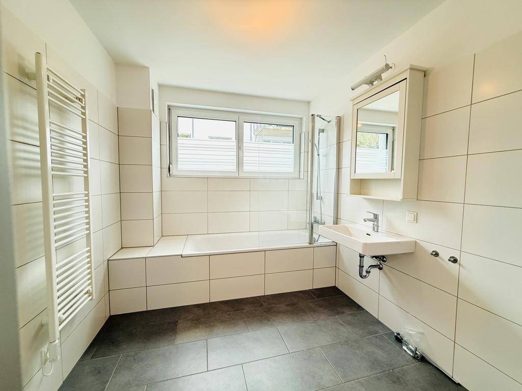 Modernes Badezimmer mit Badewanne, Dusche, Waschbecken und beheiztem Handtuchhalter.