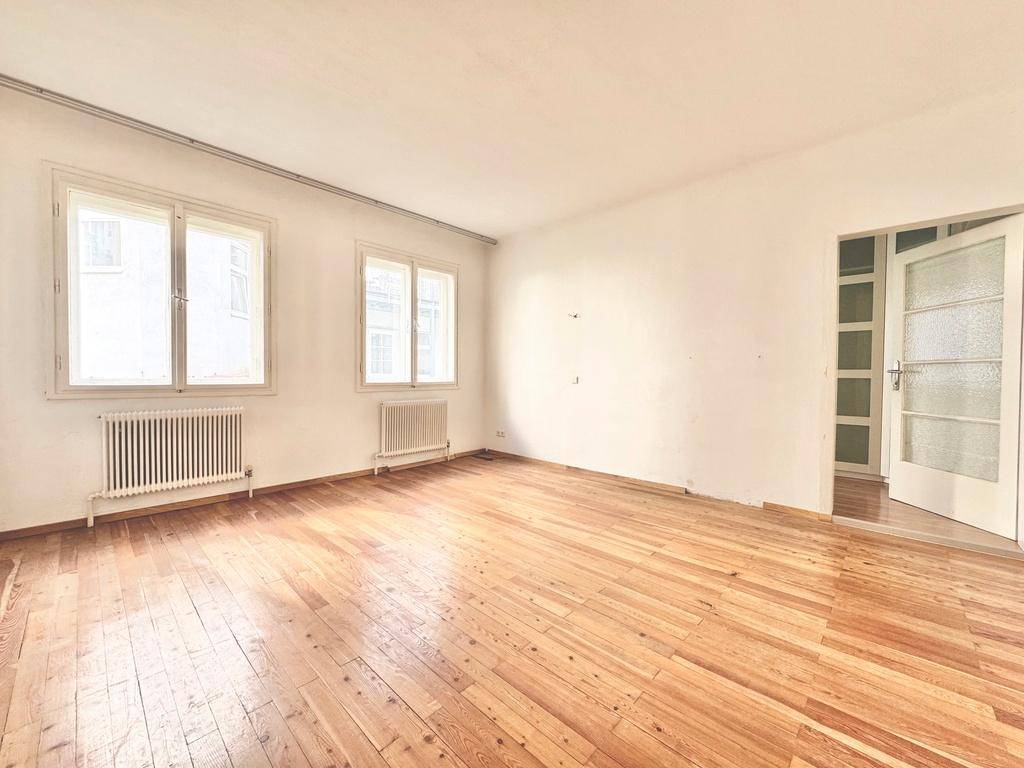 Geräumiges Zimmer mit hellem Holzboden und zwei Fenstern, die den Raum gut belichten.